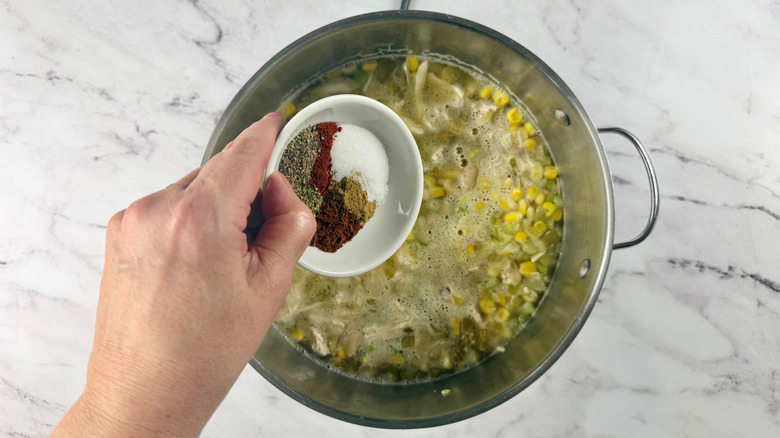 hand holding a bowl of seasonings over a metal pot