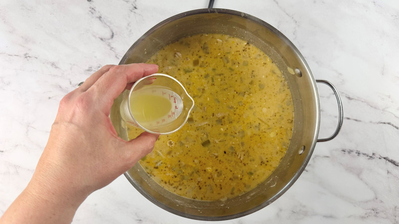 hand holding a cup of yellowish liquid over a metal pot