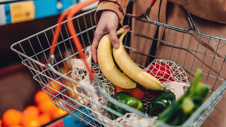A shopper places two bananas into a metal grocery basket