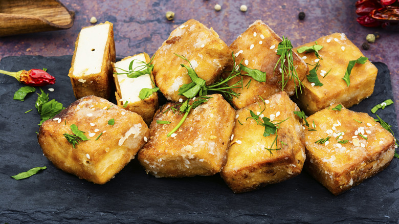 Squares of crispy tofu garnished with herbs, with one piece of tofu cut in half