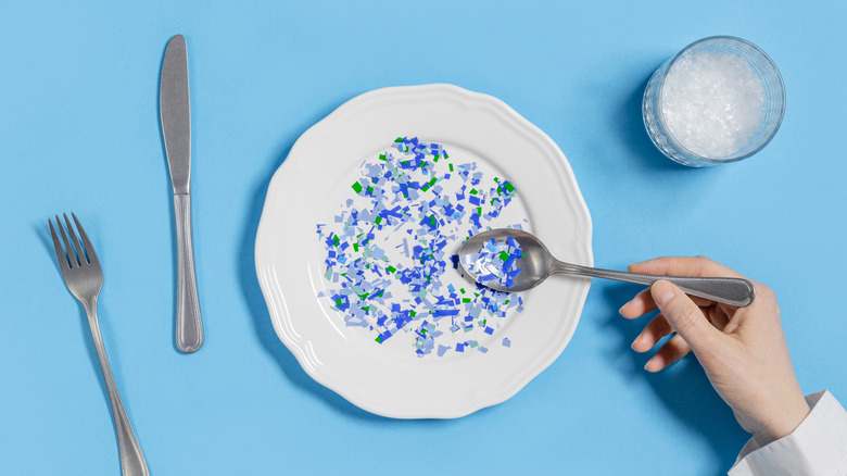A plate of small plastic pieces on a spoon instead of food with a glass of plastic nearby.