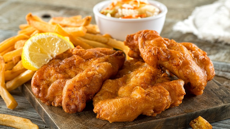 Fried fish, french fries, and coleslaw on wood board