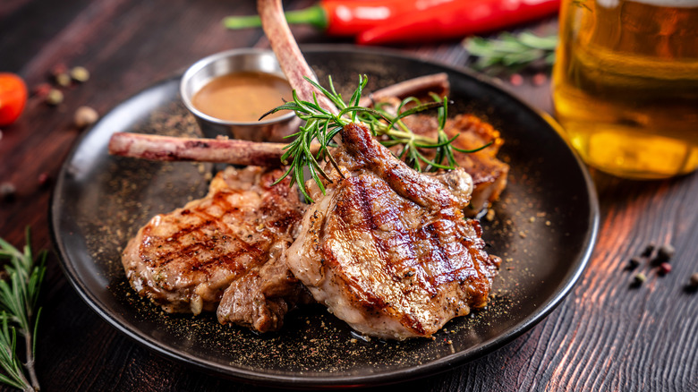 Garnished lamb chops on a black plate with seasonings and herbs.