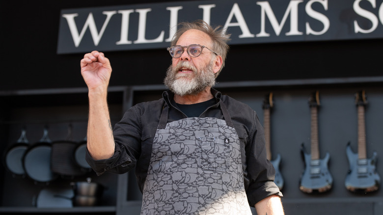 Alton Brown speaking on stage at a Williams Sonoma event with an apron on.