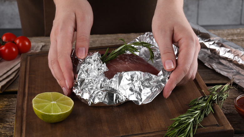 Woman wrapping meat with aluminum foil