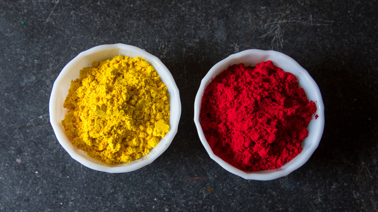 Yellow and red food dyes in small white containers placed atop a black granite surface.