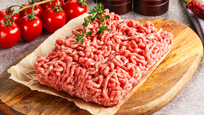 Raw ground beef on a wooden board alongside fresh tomatoes