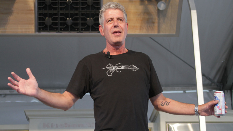 Anthony Bourdain gestures on stage with beer