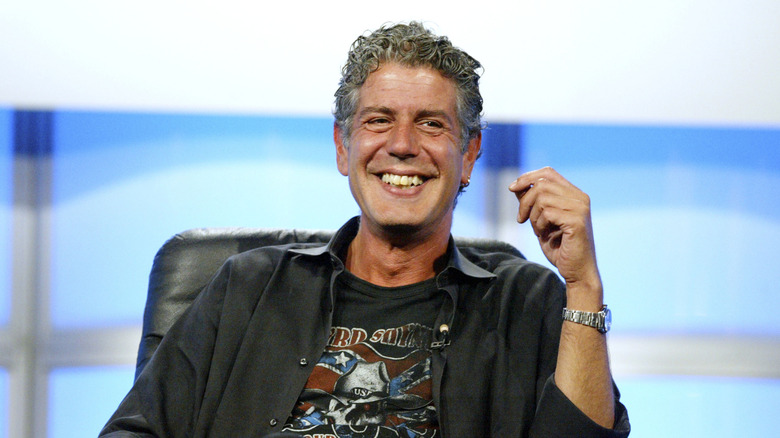 Anthony Bourdain smiling on a stage with a black jacket.