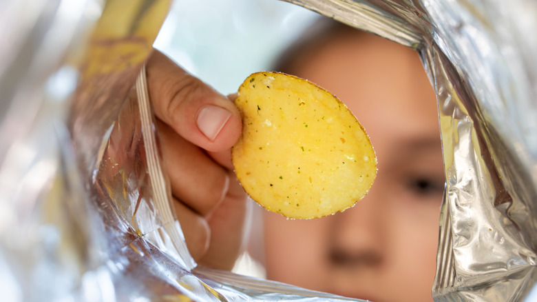 A child looks into a potato chip bag while holding a chip