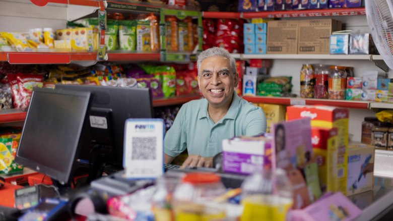 A man sits behind the cash register of his Indian grocery store