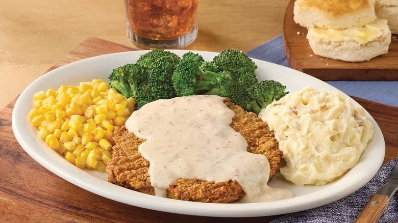 Cracker Barrel's Country Fried Steak plate on a wooden surface near biscuits and a beverage