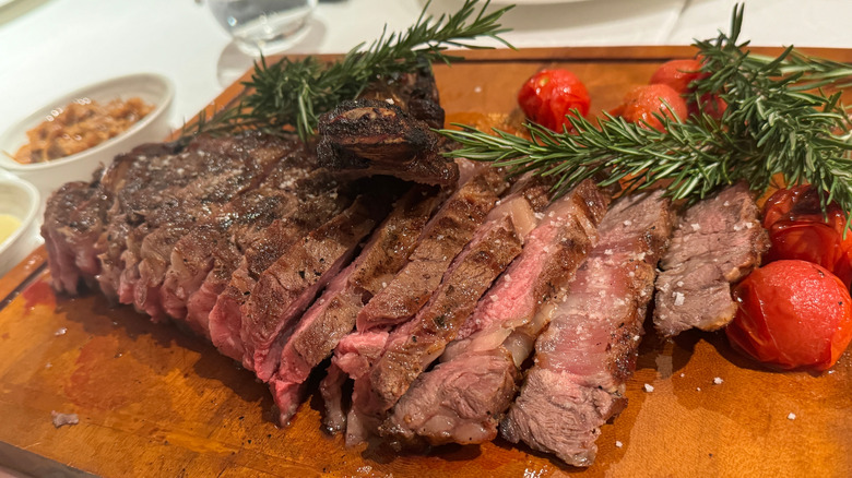 A sliced, medium-well steak with cherry tomatoes and rosemary on a wooden board