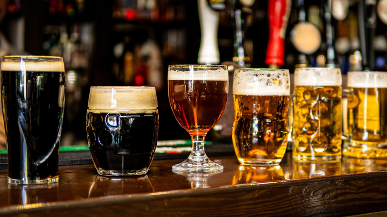 Several different beers in various types of glasses on a bar counter.