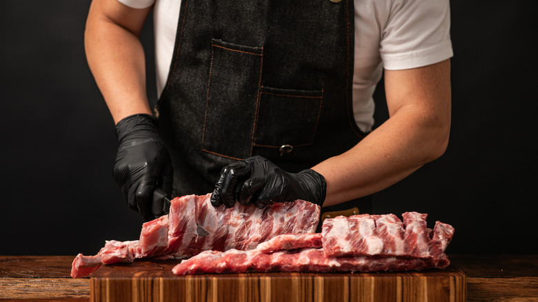 A cook prepares a rack of by slicing them into individual ribs