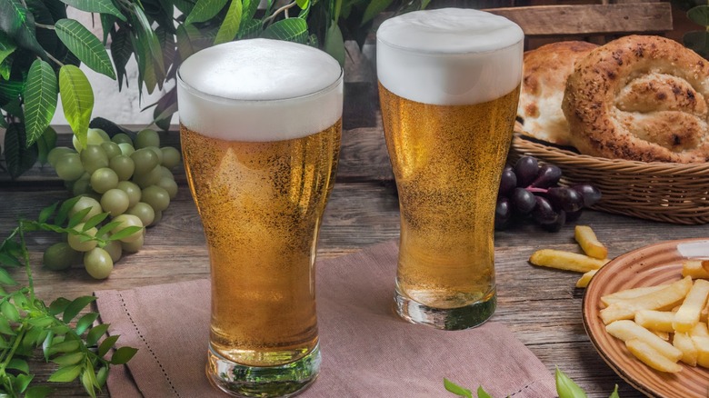 Two tall glasses of beer on a table with food