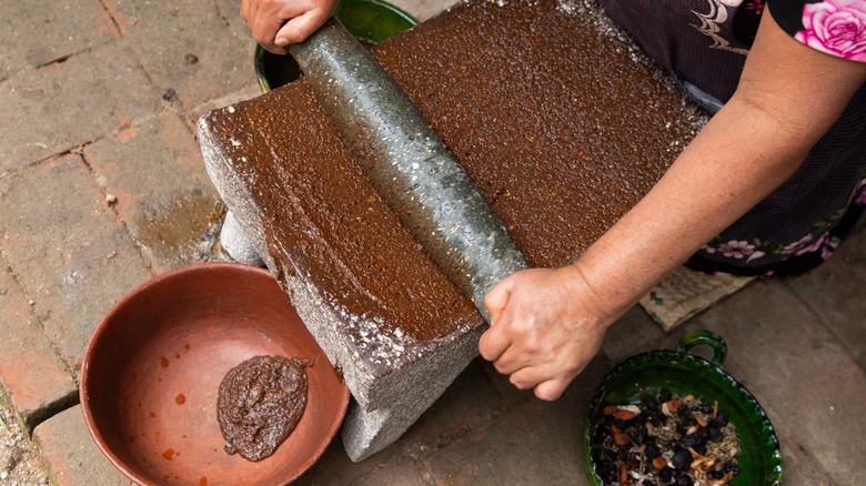 Hands grinding dark red ingredients into a paste in bowl