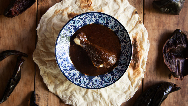 Blue and white dish with chicken leg, dark sauce on tortilla