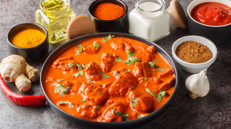 A bowl of chicken tikka masala surrounded by raw ingredients