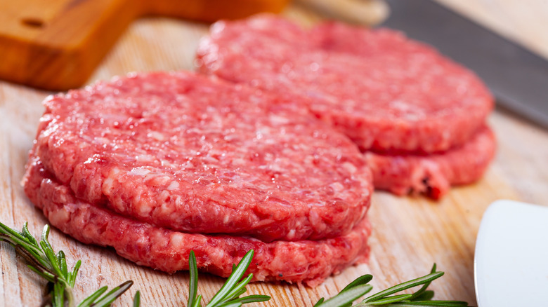 Uncooked burger patties on a wood surface with fresh rosemary