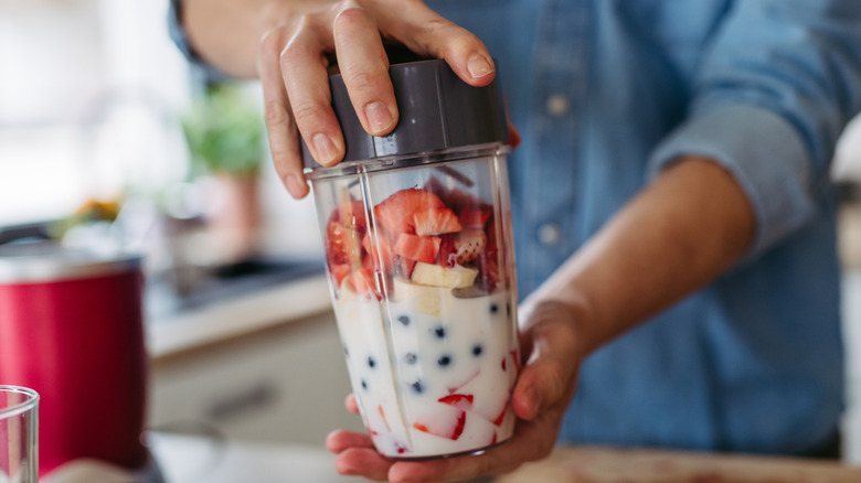 Close-up of hands holding a smoothie blender with cut strawberries, blueberries, and banana slices with milk in it