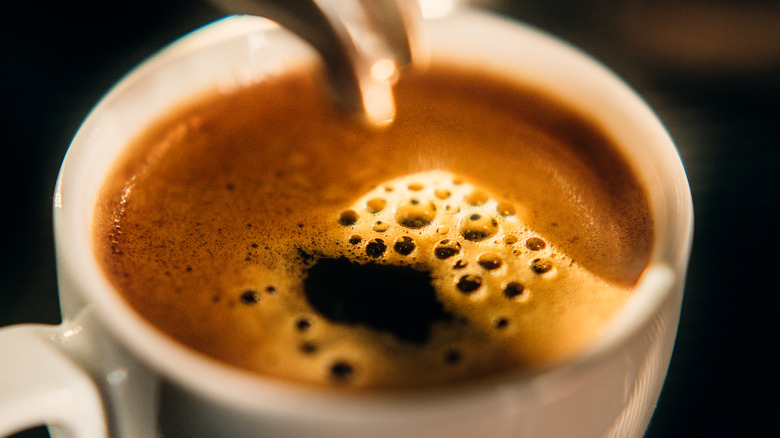 A close-up of a white mug being filled with espresso