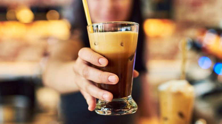 A barista holds a nitro cold brew in a glass with a straw