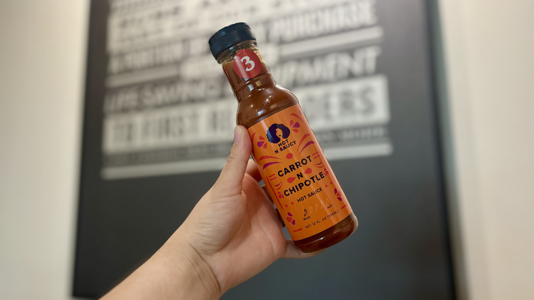 Hand holding bottle of Hot n Saucy Carrot N Chipotle hot sauce