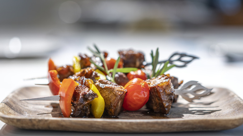 Cooked lamb skewers with bell peppers, tomatoes, and rosemary