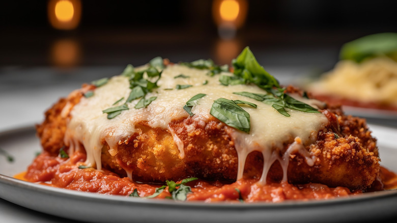 Saucy chicken parmesan with melted cheese and parsley in it at a dark restaurant