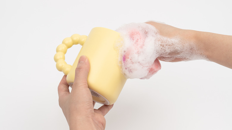 Hands scrubbing a coffee mug with a soapy sponge