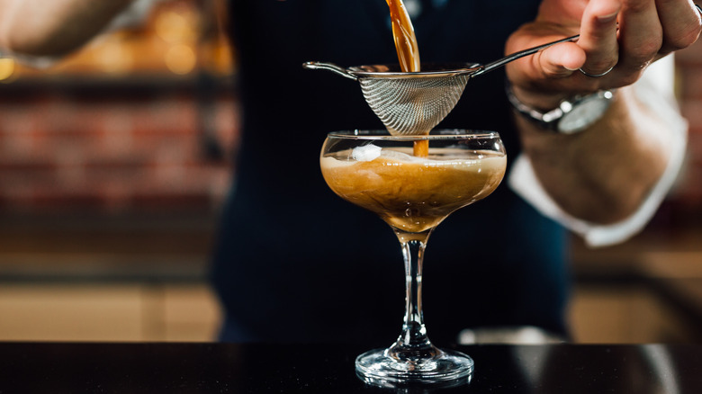 A bartender pours a coffee cocktail from a shaker into a martini glass