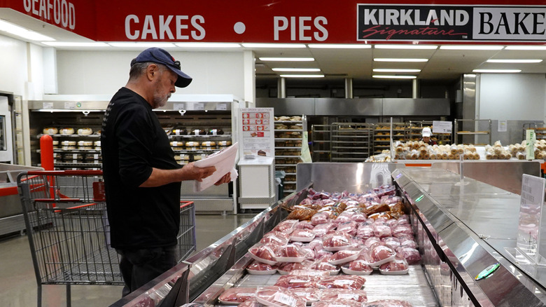 A man standing in front of the meat section at Costco looking at a package of beef.
