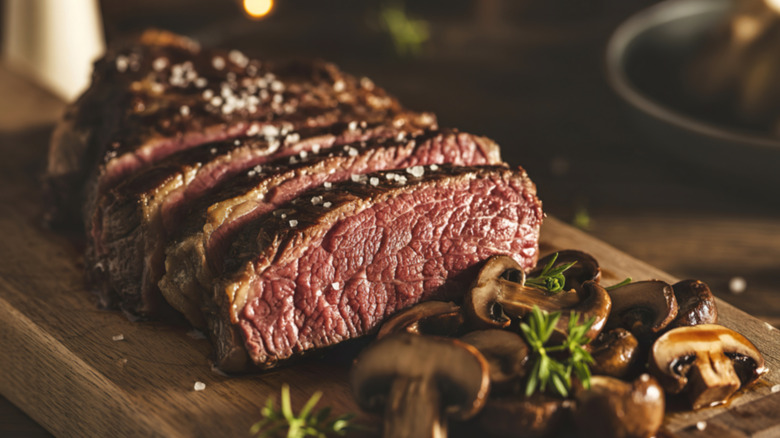 A medium rare steak on a wood cutting board with mushrooms and herbs.