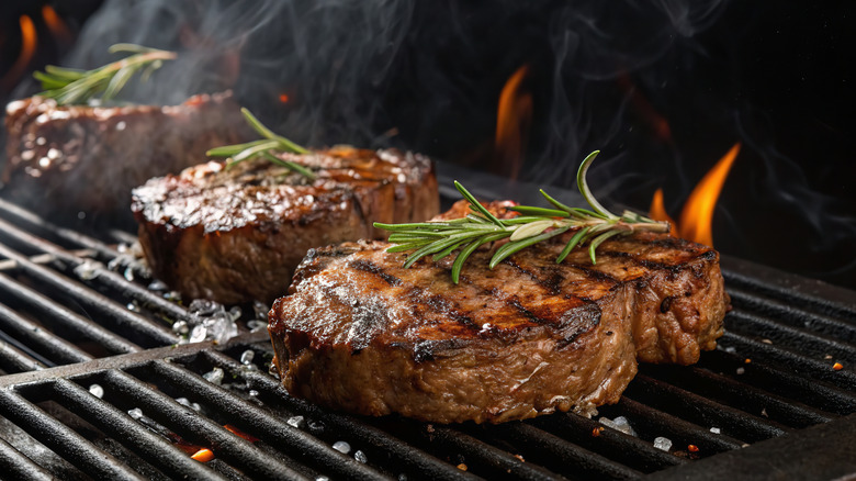 A row of thick steaks sitting on a grill with open flames coming out.
