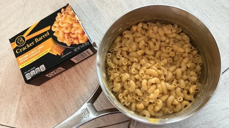 A saucepan full of Cracker Barrel mac and cheese next to a package of same.