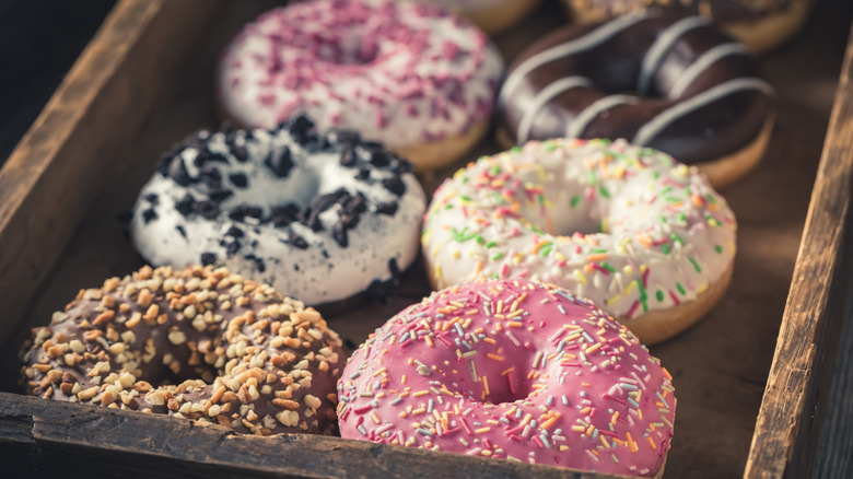 Several different donut flavors stored together in a small wooden crate.