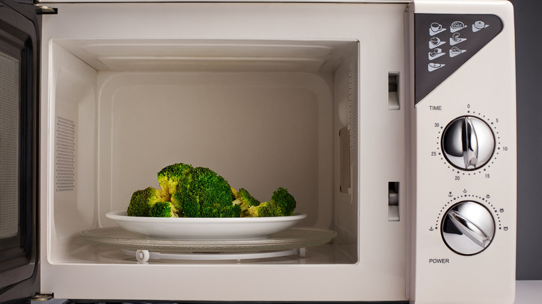 white microwave with broccoli inside on a plate