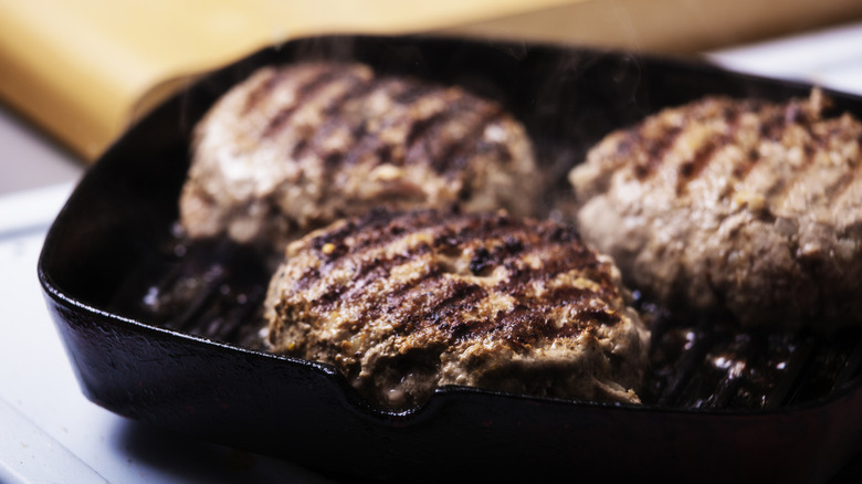 Three burgers cook in a cast iron pan