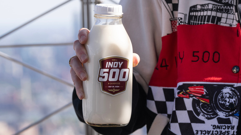 a NASCAR driver holding a bottle of milk with the 108th Indy 500 logo on it.