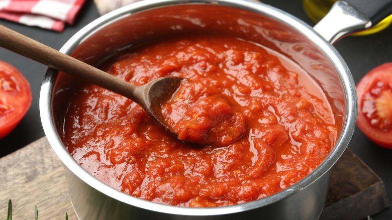 A wooden spoon scoops up tomato sauce cooking in a pot
