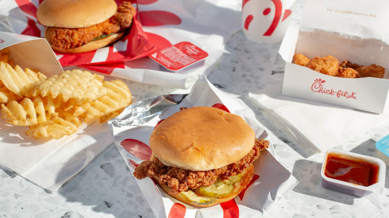 A Chick-fil-A meal featuring a classic chicken sandwich with pickles, waffle fries, chicken nuggets, dipping sauces, and a drink.
