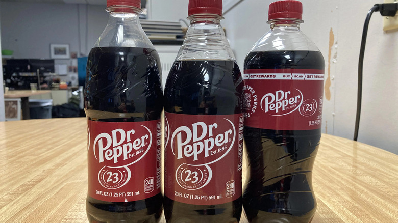 Three differently-shaped bottles of Dr Pepper on a wooden table.