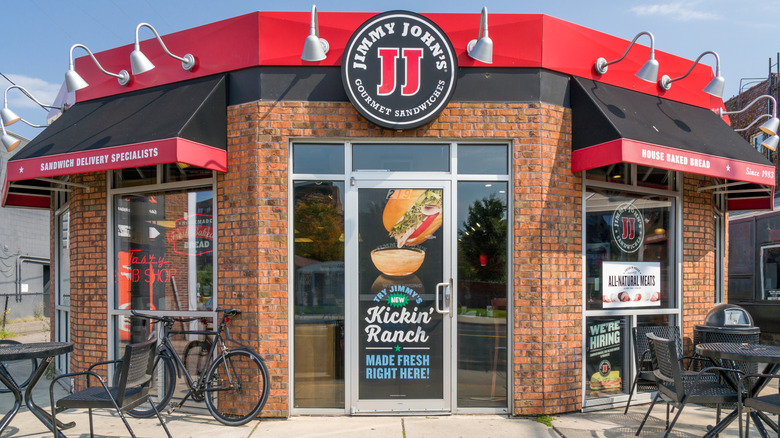 A red brick Jimmy John's location with tables and chairs and a bicycle outside.