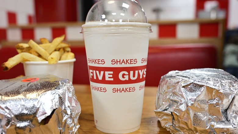 A meal at Five Guys sitting on a table, including two burgers, a shake, and fries.