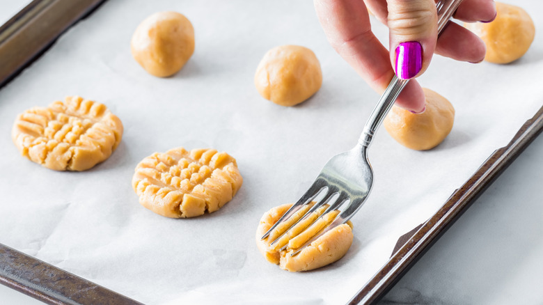 Hand flattening peanut butter cookie dough with fork