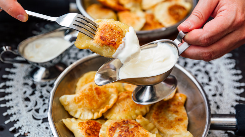 Someone dipping a potsticker into sour cream