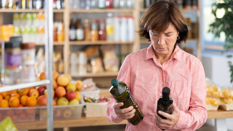person in pink shirt comparing olive oils in supermarket