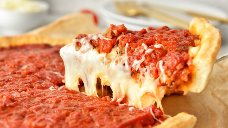 Person lifting a slice of Chicago-style deep dish pizza with cheese pull