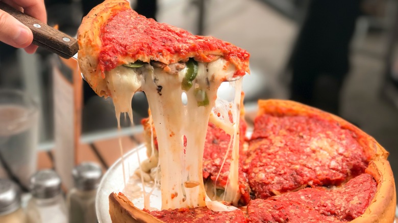 Person lifting a slice of Chicago-style deep dish pizza with extended cheese pull